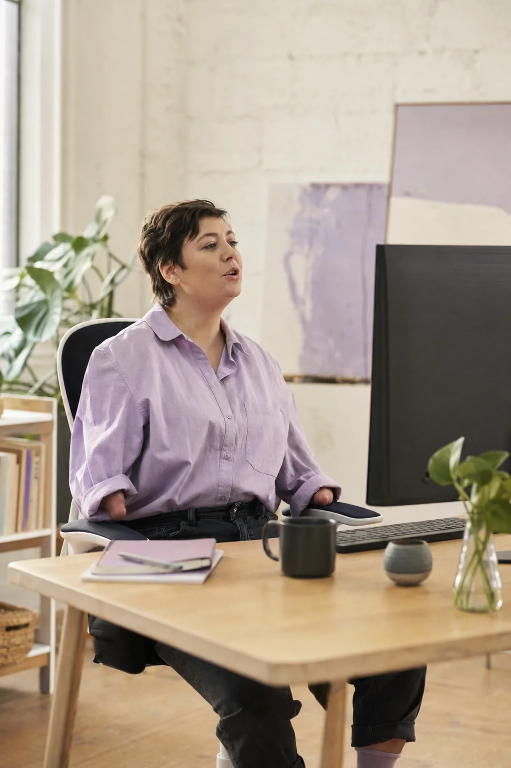 A professional with limited hand mobility speaking toward a desktop computer in a bright studio
